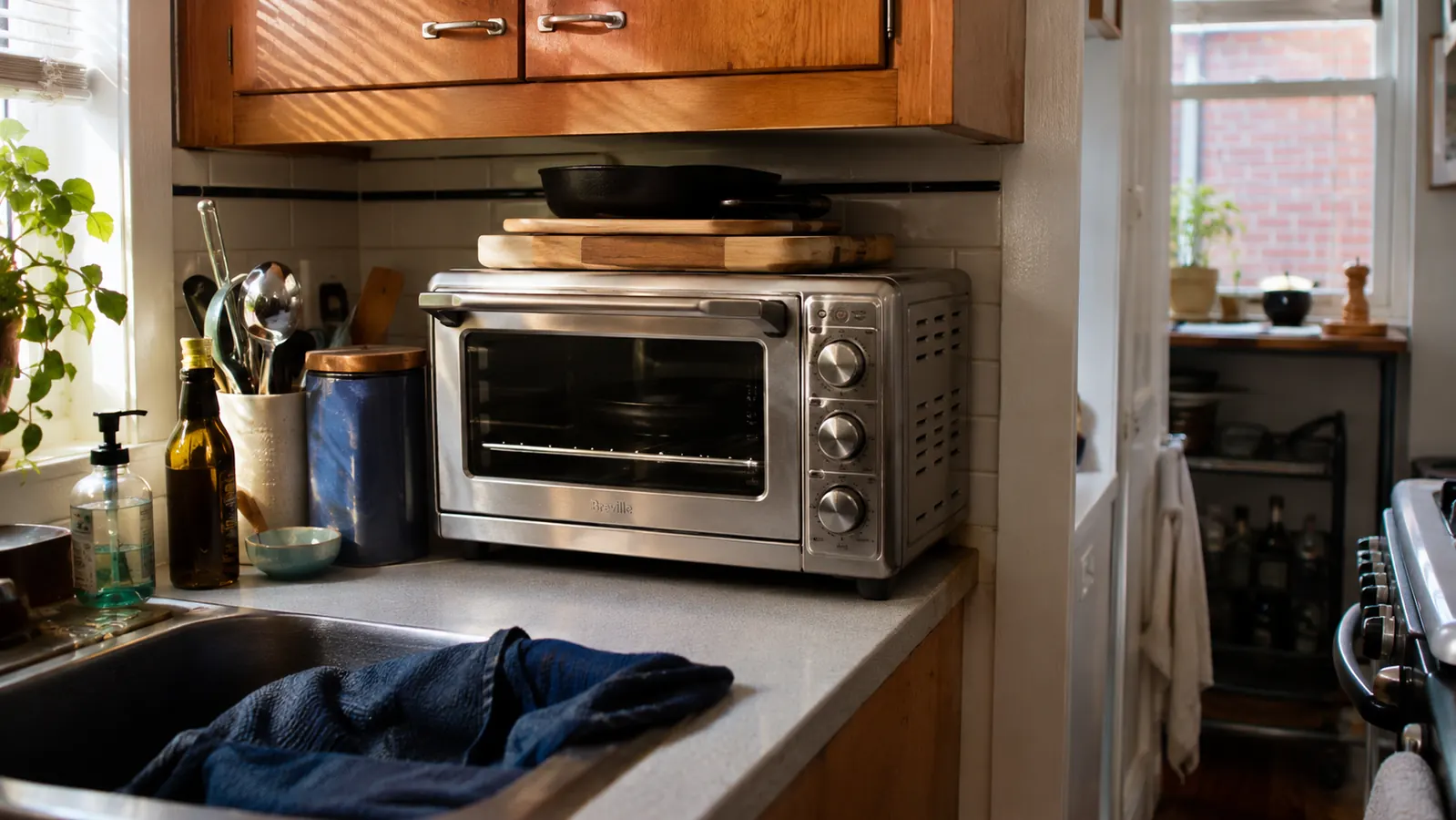 A silver BLACK+DECKER toaster oven sitting on a narrow kitchen counter next to a coffee maker, with an upper cabinet close overhead
