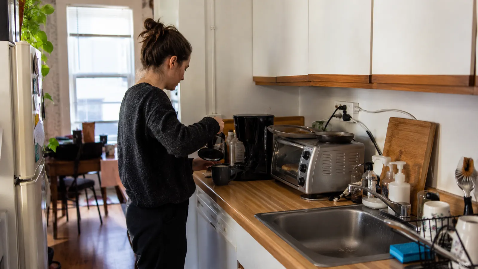 Silver BLACK+DECKER toaster oven on a narrow strip of counter beside a kitchen sink, cord running to a shared power strip