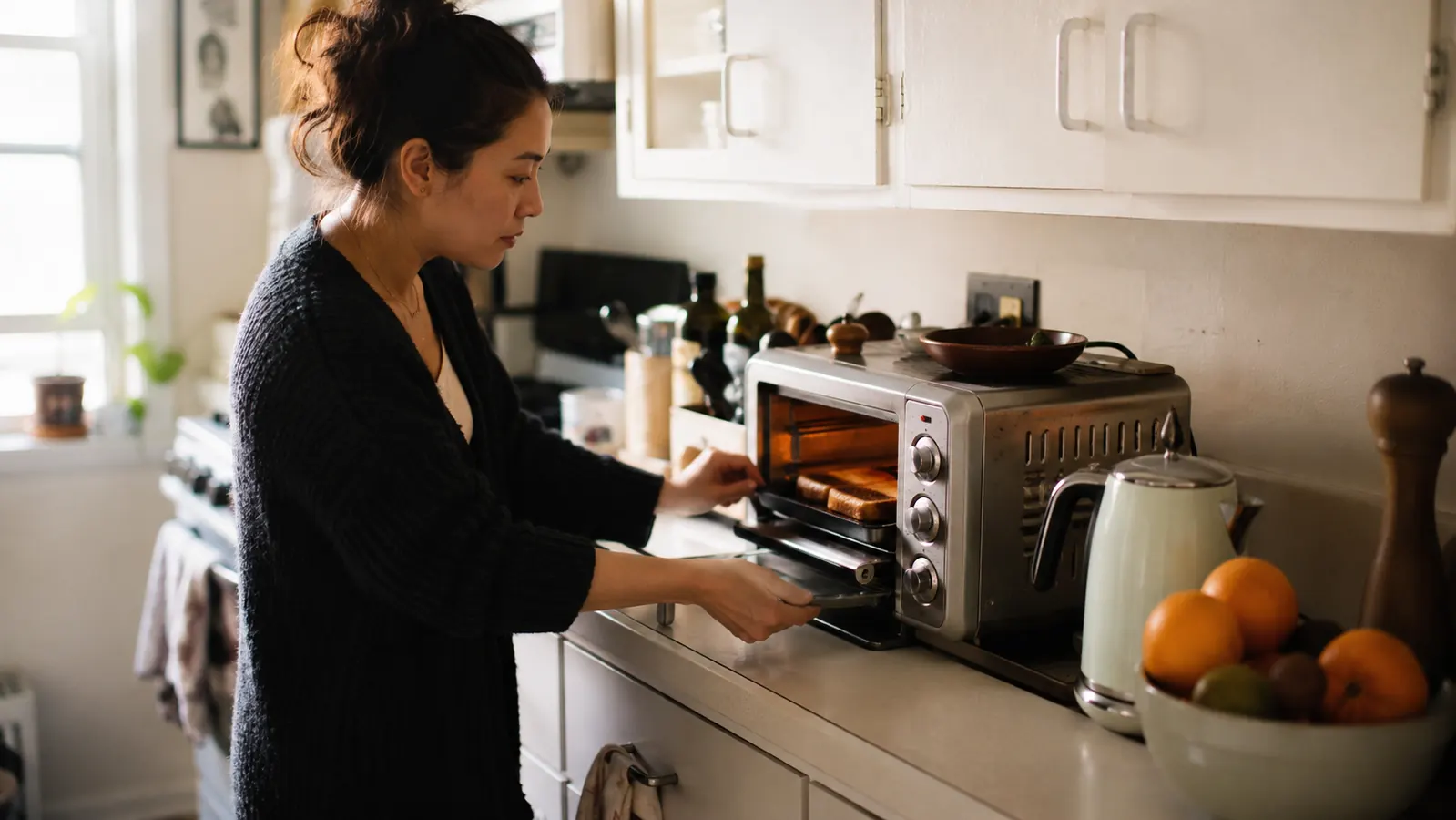Silver BLACK+DECKER toaster oven sitting on a narrow kitchen counter next to a coffee maker, morning light coming through a window