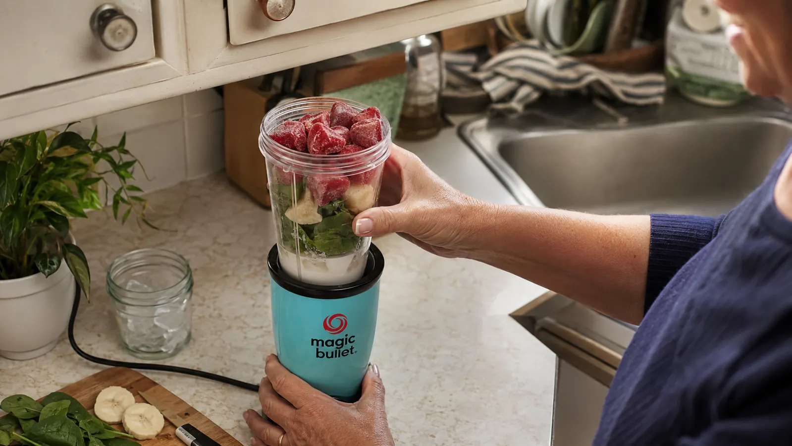 Overhead view into a Magic Bullet cup showing liquid on the bottom, soft fruit in the middle, and frozen fruit chunks on top before blending