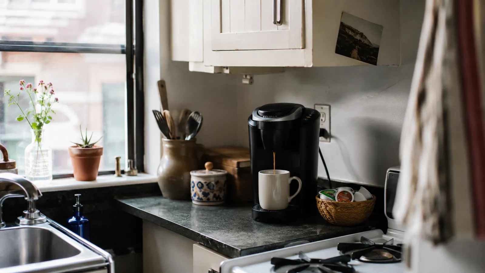 Keurig K-Express coffee maker sitting on a narrow kitchen counter beside a mug and a small stack of K-Cup pods