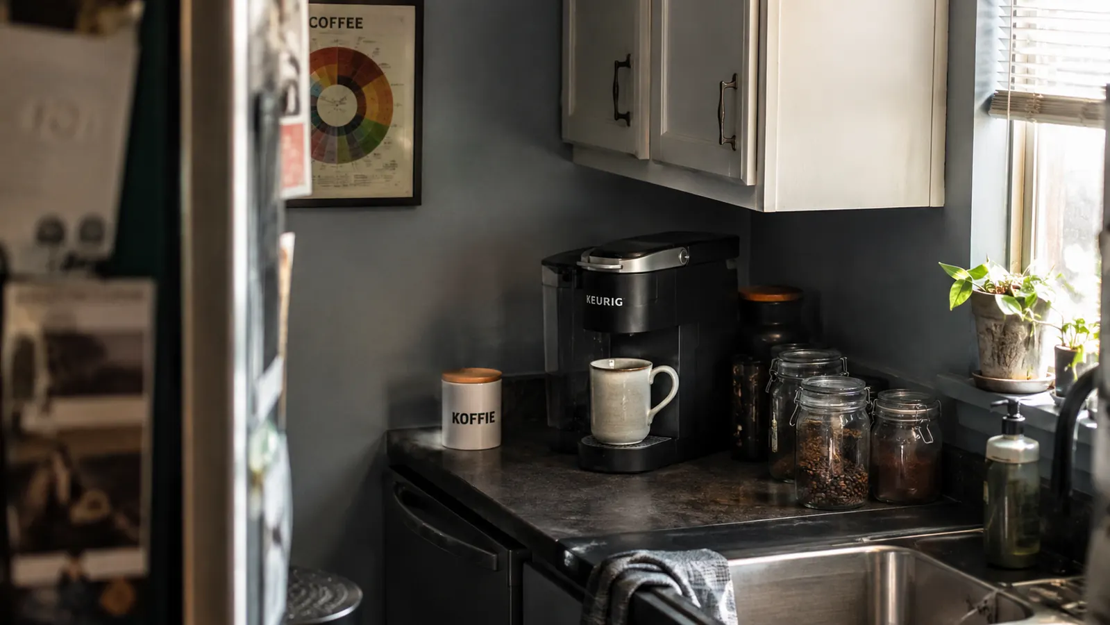 A compact single-serve coffee maker sitting in the corner of a narrow kitchen counter with morning light coming through a nearby window
