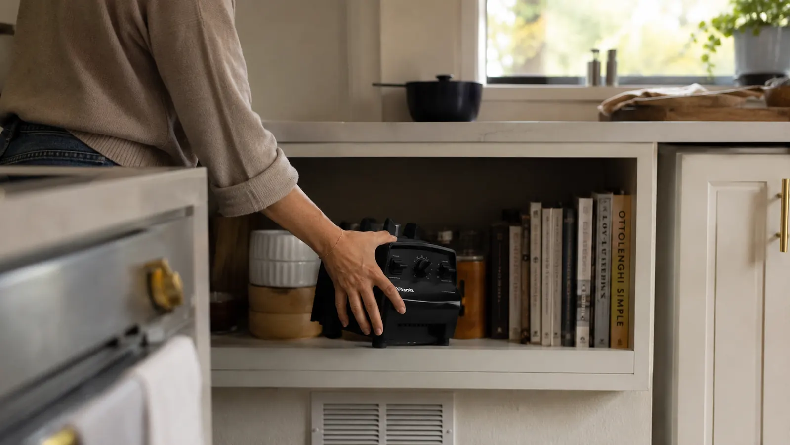 Close view of the blender base and cups stored on a low shelf beside the coffee maker, being lifted down