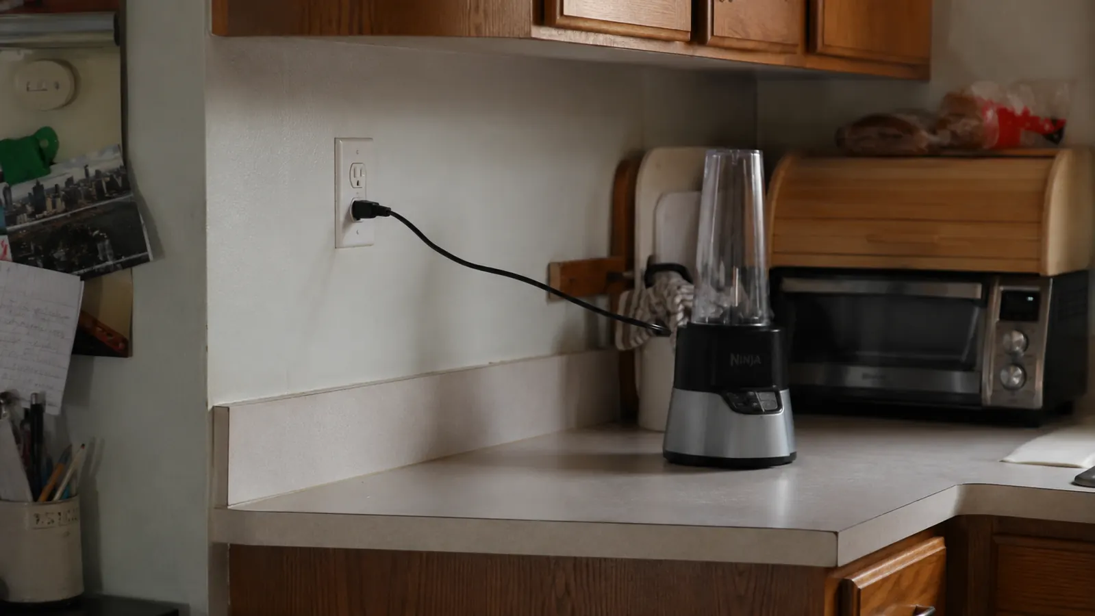 Short power cord stretched taut from a wall outlet to the blender base on a kitchen counter near a toaster oven