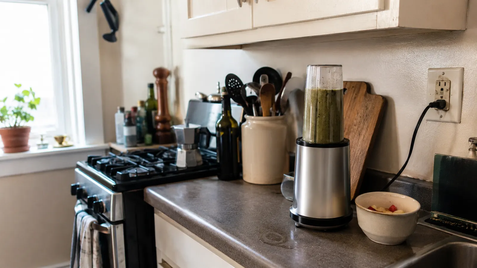 Small silver personal blender on a narrow apartment counter with a faint water ring beside the base