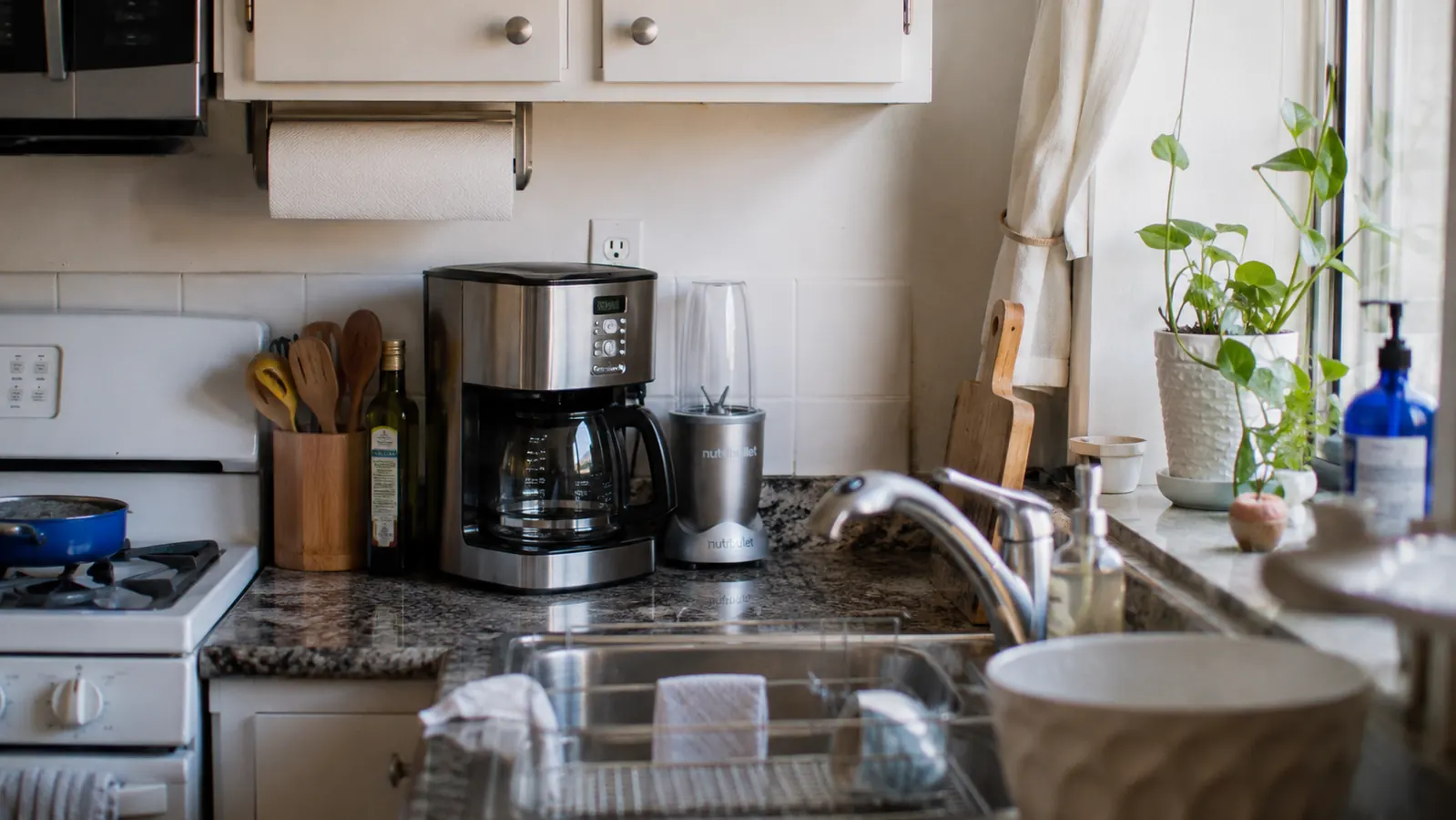 Small silver Magic Bullet blender sitting on a narrow apartment kitchen counter next to a coffee maker